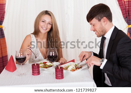 Young couple seated at a restaurant table enjoying a romantic dinner by candlelight and drinking red wine