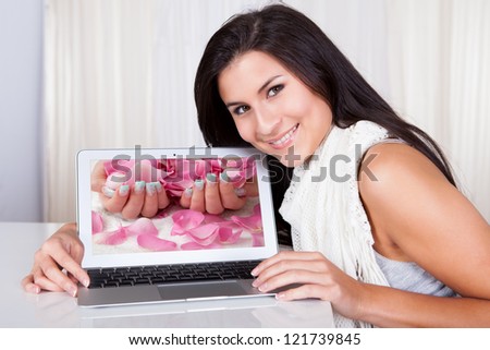 Happy woman looking for fingernail designs on her laptop at home