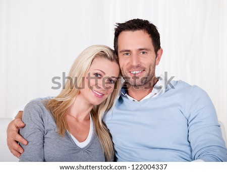 Affectionate couple relaxing on a sofa with the mans arm around his wifes shoulders as she rests her head on his shoulder