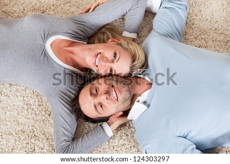 Happy relaxed attractive man and woman lying on their backs head to head on a white carpet smiling up at the camera