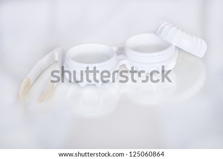 A pair of tweezers lies alongside an open contact lens storage case with the lenses in a sterile solution with copyspace