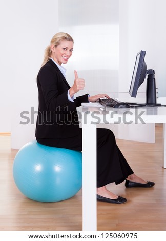 Comfortable working environment with an elegant young blonde office worker sitting on a pilates ball