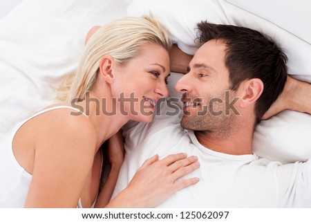 Loving couple lying in bed gazing into each others eyes as they lie back on the pillows