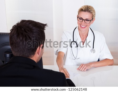 Attractive female doctor wearing glasses and a stethoscope consulting with a male patient with his back to the camera