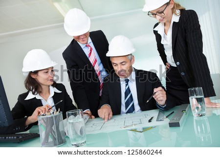 Meeting of four diverse architects or structural engineers in hardhats and suits seated in an office