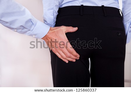 Conceptual image of harassment in the workplace with a man stretching out his hand to touch a colleagues bottom