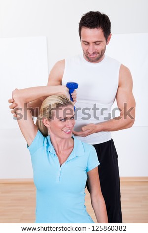 Fitness instructor helping a woman with her workout guiding her arm behind her head as she lifts dumbbells