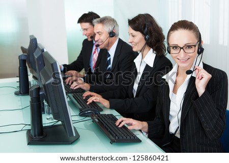 Line of professional stylish call centre operators wearing headsets seated behind their computers giving assistance