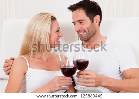 Casual attractive couple relaxing at home toasting each other with large glasses of red wine