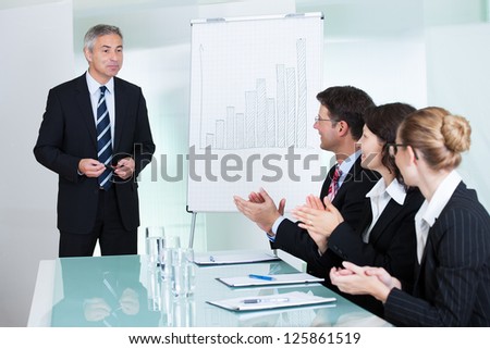 Diverse business colleagues seated around a table clapping after a staff presentation by a manager or senior executive