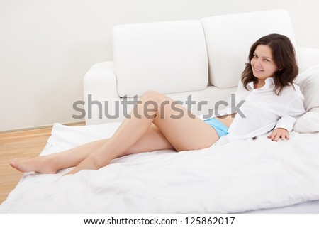 Beautiful natural woman with a gentle smile sitting on her bed with her knees clasped in her arms