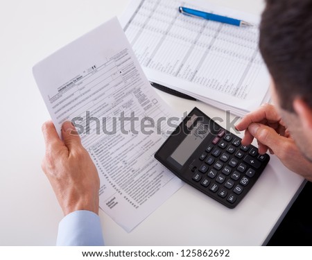 Over the shoulder view of a man checking an invoice on a calculator