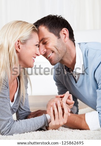 Young couple watching each other gazing into each others eyes with love while lying on their stomachs on a white carpet
