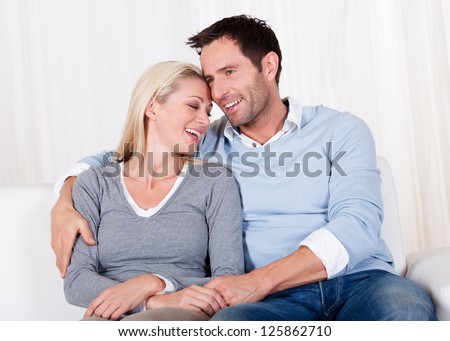 Romantic young couple expressing their love by rubbing noses as they sit close together on a sofa