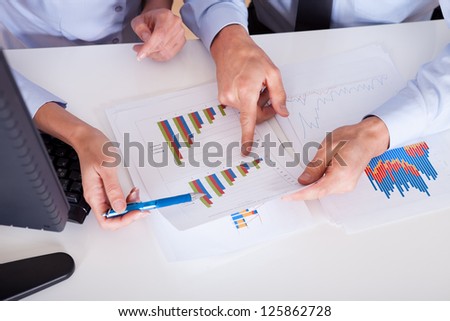 Smiling business colleagues sitting behind a desk discussing statistics with bar graphs in their hands