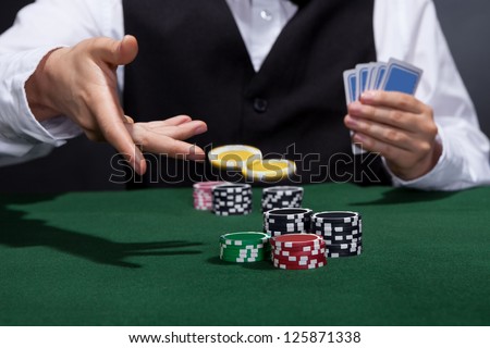 Poker player increasing his stakes throwing tokens onto the gaming table to meet or beat his opponents wager to stay in the game