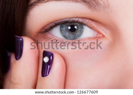 Closeup of a natural beautiful blue-grey female eye with fingertips showing manicured purple nails below