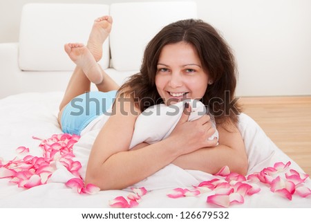 Smiling natural woman lying on a bed with her feet in the air surrounded by rose petals