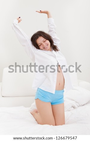 Attractive young woman kneeling on her bed stretching after waking up in the morning