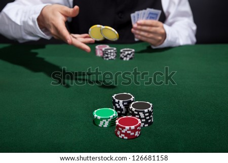 Poker player increasing his stakes throwing tokens onto the gaming table to meet or beat his opponents wager to stay in the game