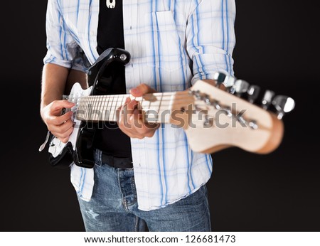 Young guitar player singing. Dark background. Selective focus