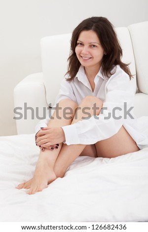 Beautiful natural woman with a gentle smile sitting on her bed with her knees clasped in her arms