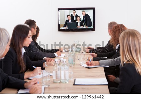 Businesspeople Sitting At Conference Table Looking At Flat Screen Display