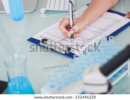 Close-up Of Female Scientist Writing On Notepad