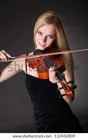 Beautiful young woman playing violin over black background