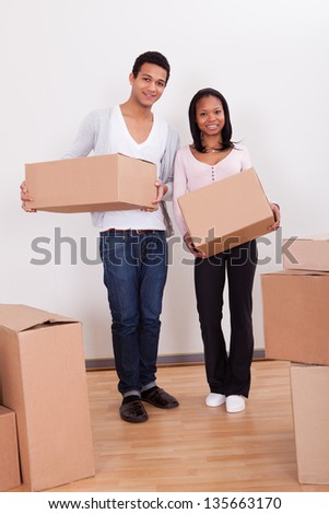 Portrait Of Young Couple Carrying Boxes In House