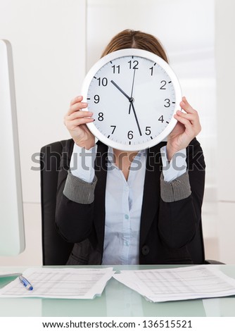 Businesswoman Holding Clock In Front Of Her Face In Office