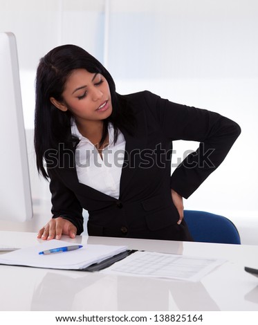 Young Businesswoman Sitting On Chair And Holding Her Back In Pain