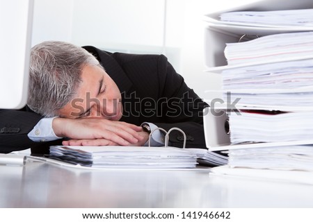 Tired Mature Businessman Sleeping At Desk In Office