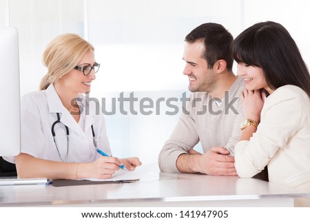 Happy Doctor Discussing With Couple In Clinic