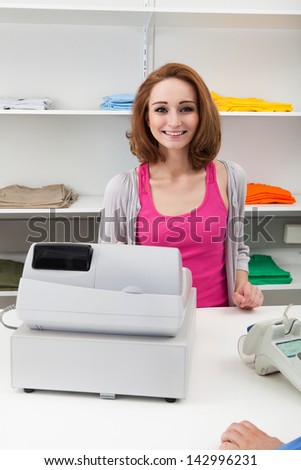 Happy Young Female Cashier With Cash Register At Cash Counter