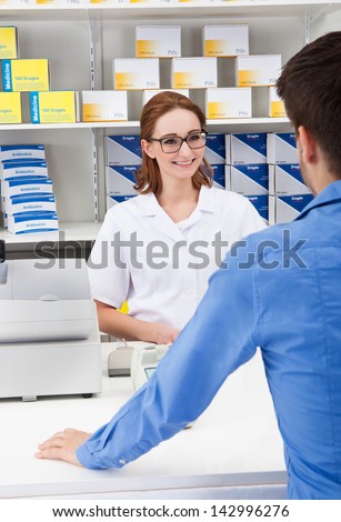 Happy Young Female Pharmacist In Pharmacy With A Client