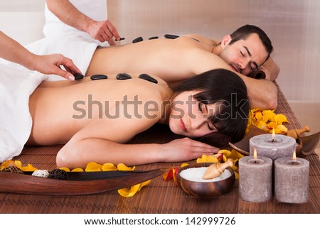 Beautiful Young Couple Enjoying Hot Stone Therapy In Spa Centre