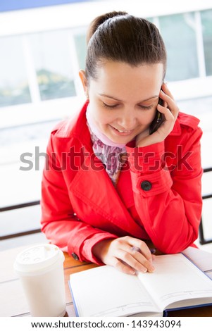 Happy woman looking at diary and talking on cell phone in restaurant