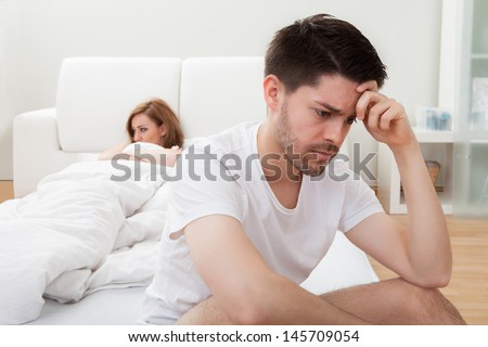 Depressed Man Sitting On The Edge Of The Bed In Bedroom