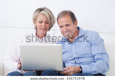 Happy Mature Couple Sitting On Couch And Working On Laptop
