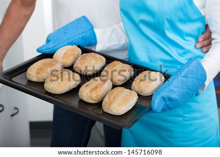 Man Looking At Woman Taking Baking Tray Out From Oven