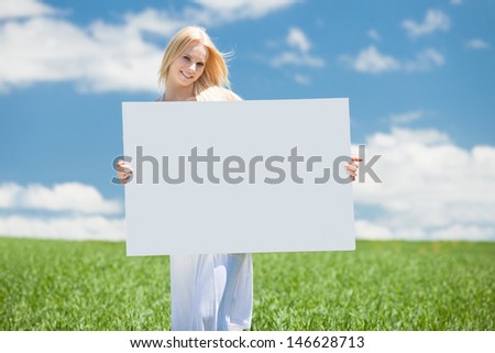 Happy Young Woman Standing In Field Holding Placard