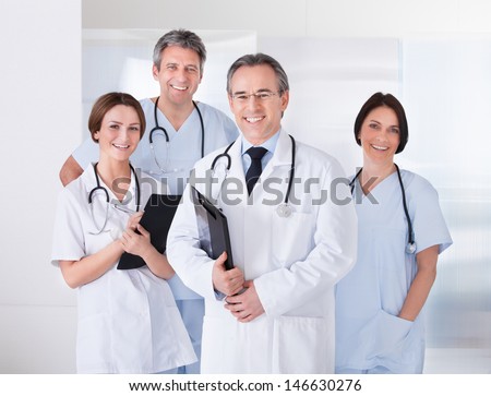 Male Doctor Standing In Front Of Team Using Digital Tablet