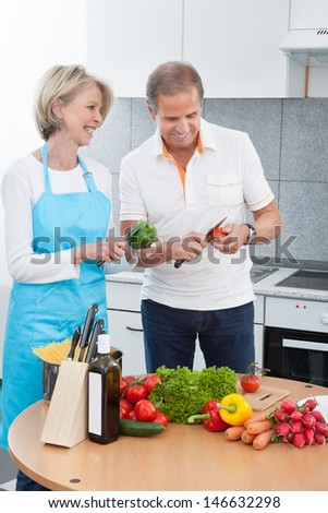Mature Man And Woman Cutting Vegetable In Kitchen