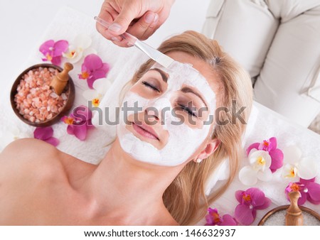 Cosmetician Applying Facial Mask To The Face Of Young Beautiful Woman In Spa Salon