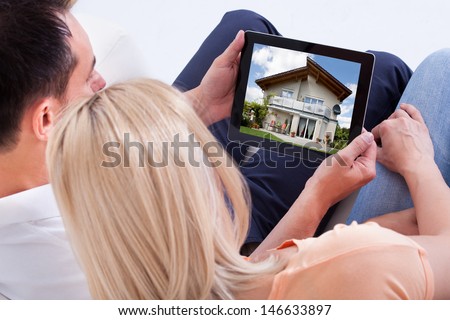 Couple Looking At House On Digital Tablet\'S Screen
