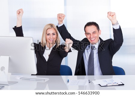 Excited Businessman And Businesswoman Raising Hands At Office