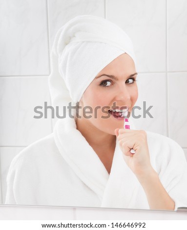 Young woman looking at mirror brushing teeth