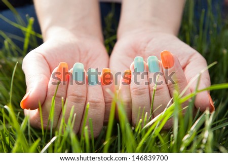 Close Up Of Woman\'s Hand With Colorful Nail Varnish On Grass