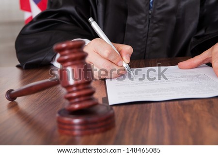 Close-Up Of Male Judge Writing On Paper In Courtroom